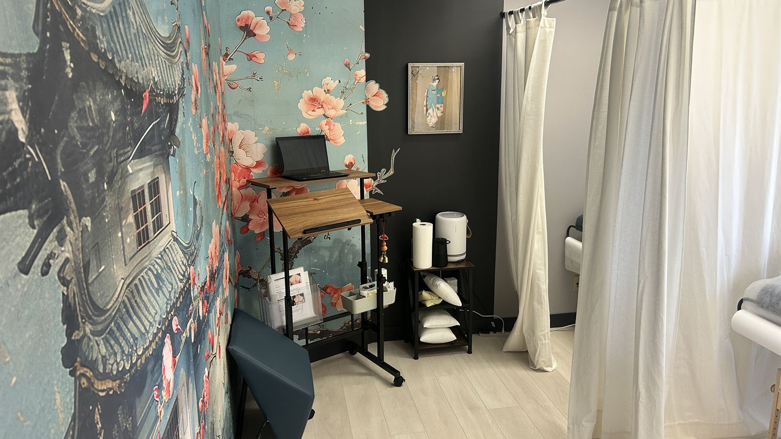 Treatment room at Aculosophy with a cherry blossom wall mural, a standing desk and white curtains around the treatment table