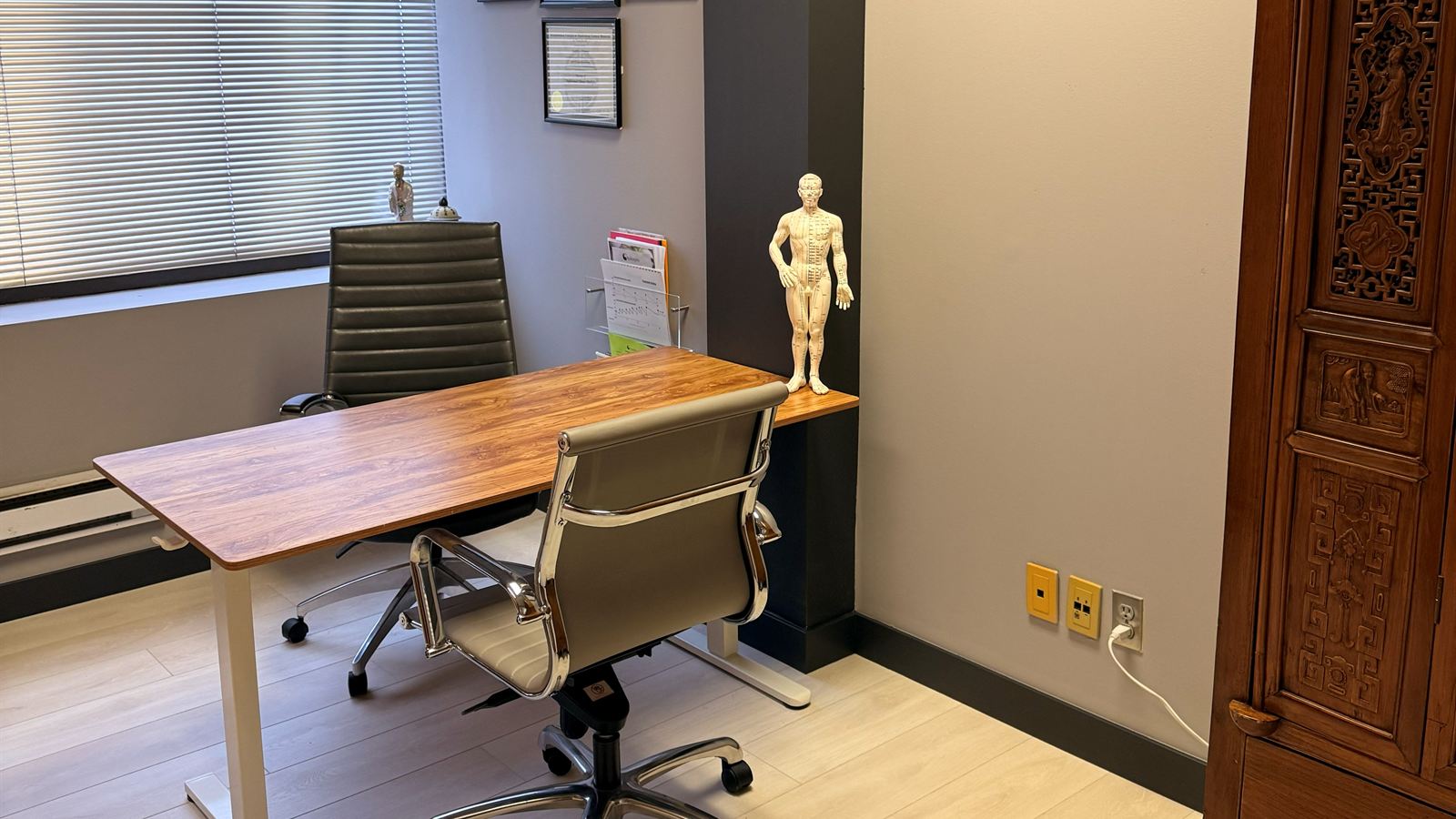 The exam room at Aculosophy with a desk, an anatomy model and a carved wooden cabinet